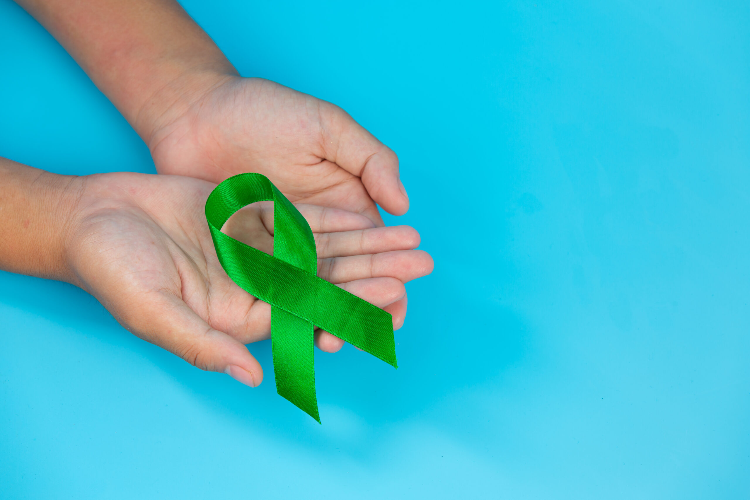 mãos segurando um laço verde para representar o abril verde